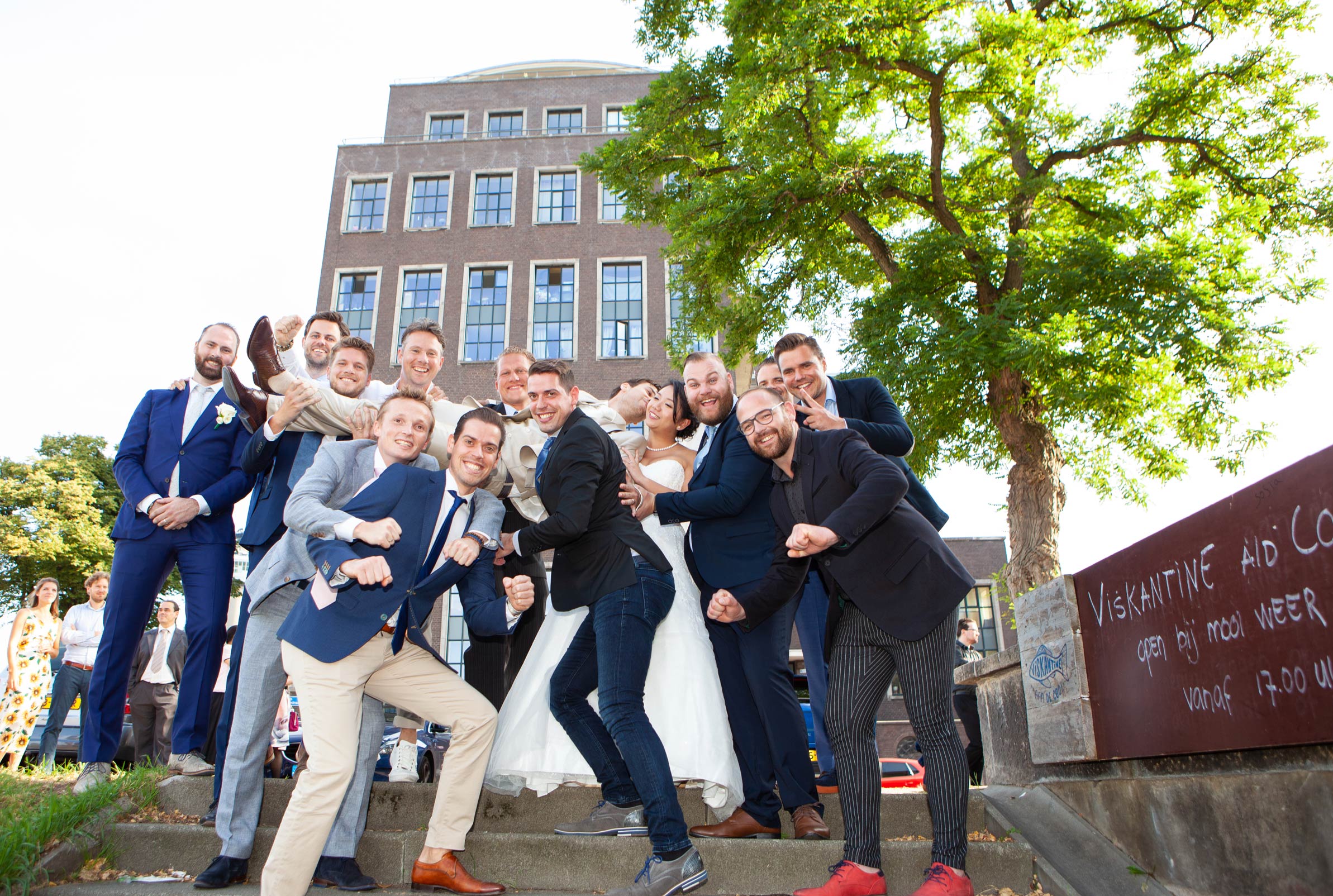 vrolijke originele en spontane groepsfoto bruiloft bruiloftsgasten met bruidspaar De Machinist Rotterdam trouwfotograaf Irene Den Haag